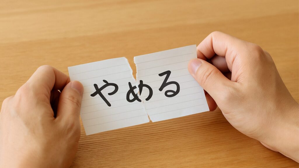 木のテーブルの上で、紙に書かれた「やめる」という文字を静かに破る手元。何かを手放す決意と新しい始まりを象徴する“やめる習慣”のイメージ。